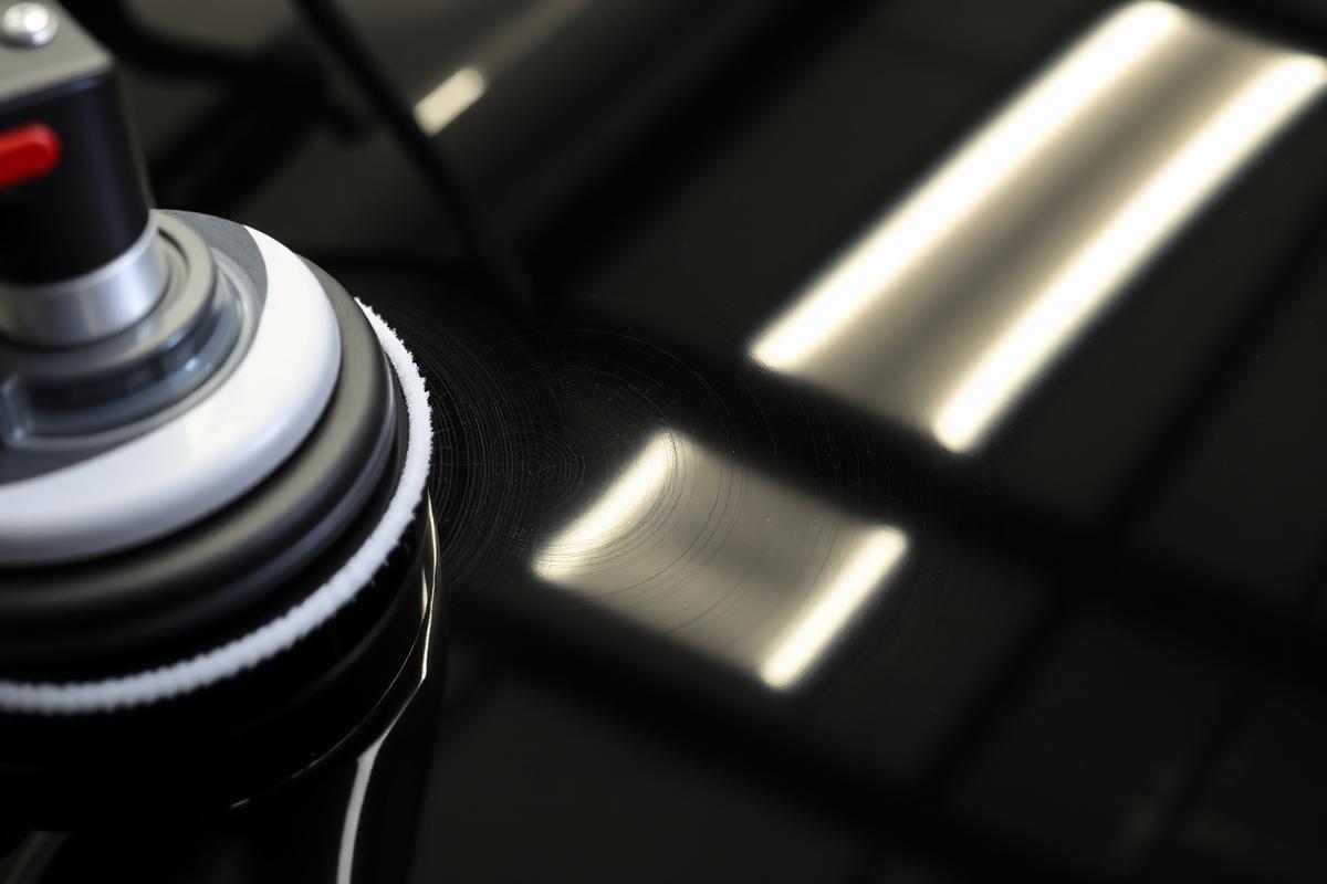 Dual action polisher removing swirl marks from black car paint under inspection lighting